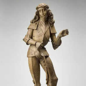 Sculpture en bois : homme debout légèrement déhanché, versant de l’eau sur une forteresse à ses pieds. Vue de face.