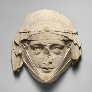 Sculpture en pierre représentant un visage féminin (nez manquant), portant un voile retenu par une fine couronne et une guimpe. Vue de face.