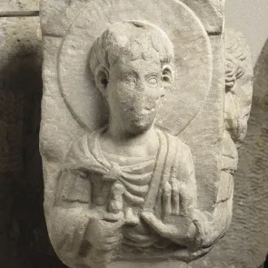 Chapiteau en pierre représentant un saint militaire en buste, le pommeau de son épée en main. Vue de face.