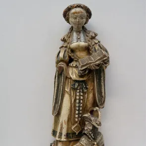 Polychrome wooden sculpture: a standing woman holding an open book and stepping on a man lying on the ground. Front view.