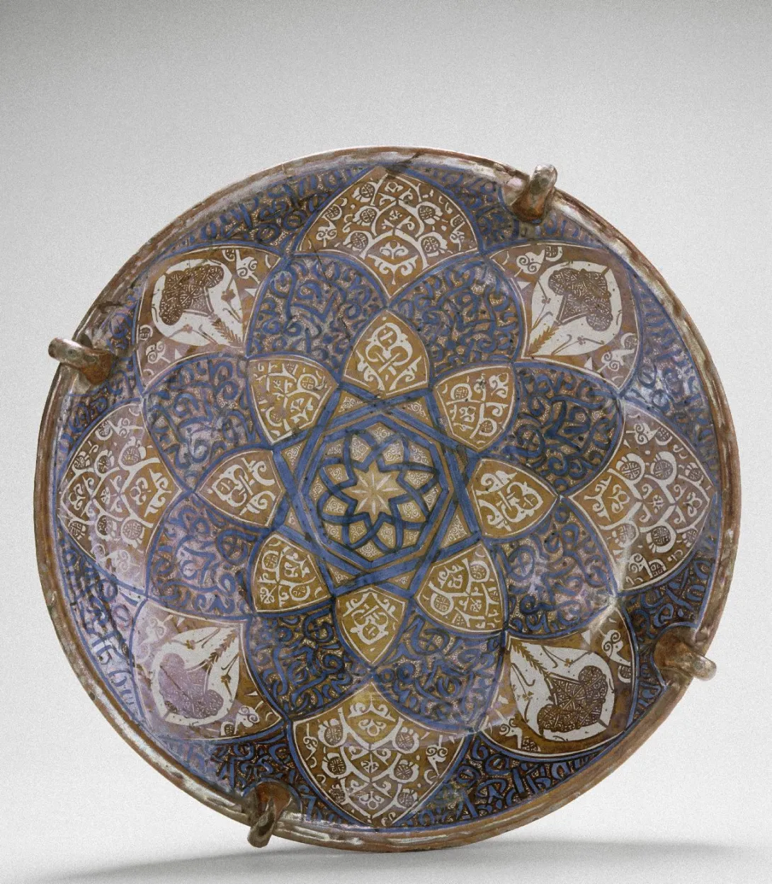 Plat rond en céramique à décor de style islamique bleus et dorés à reflet métallique. Vue de face sur fond neutre.
