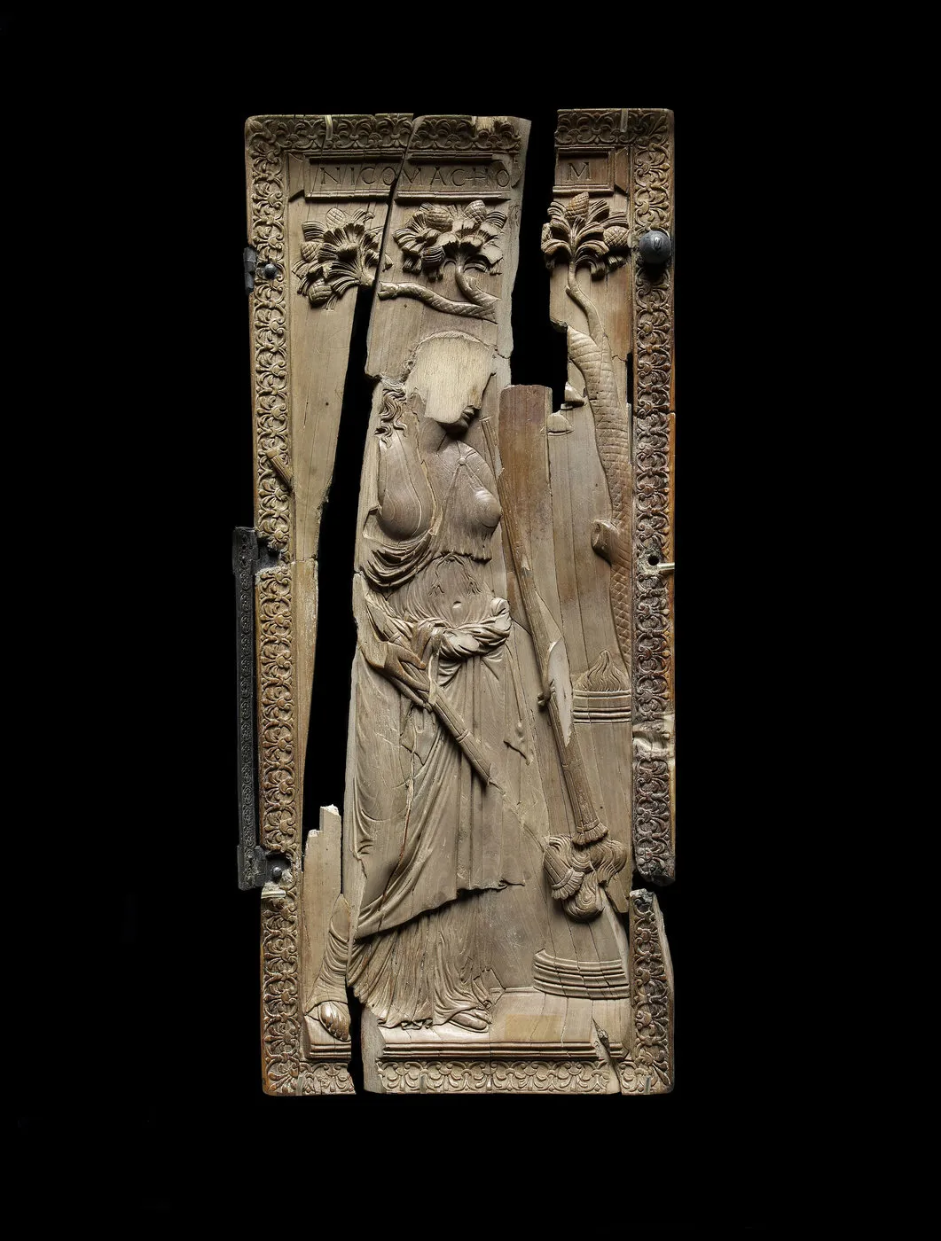 Plaque d’ivoire sculpté lacunaire représentant une femme de profil sous une branche de pin. Photographie de face.