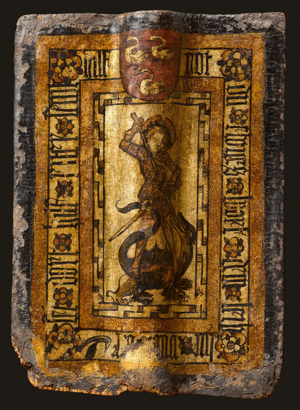 Pièce de bois peint : homme auréolé combattant un dragon, écu armorié au-dessus, encadré d’une inscription. Vue de face.