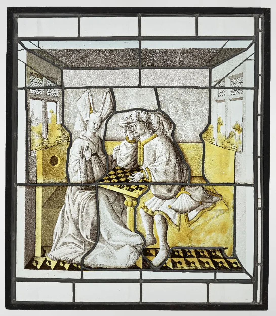Vitrail rectangulaire jaune et gris représentant un couple jouant aux échecs dans un intérieur. Vue de face. 