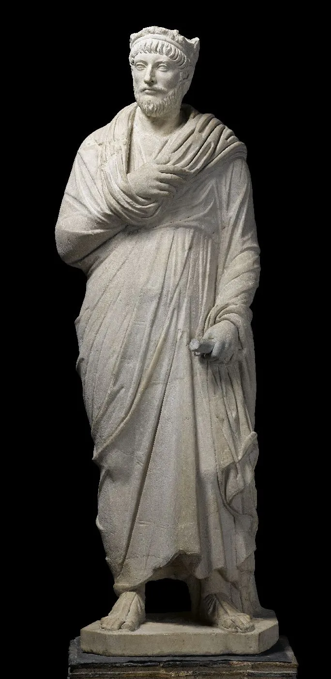 Sculpture en pierre représentant un homme drapé dans une toge antique, main gauche repliée et barbe courte. Vue de face.