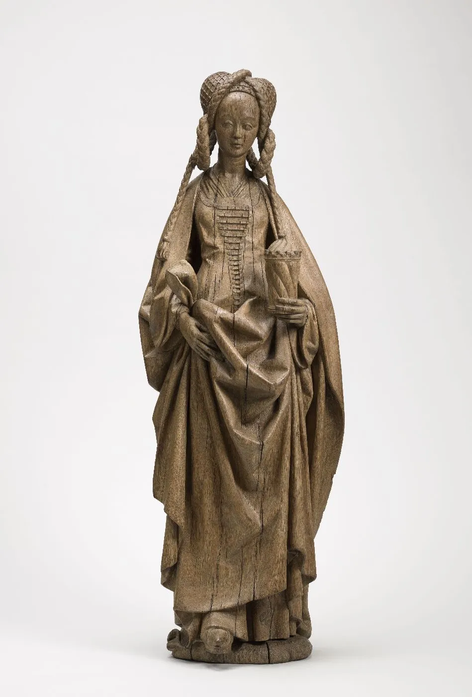 Sculpture en bois : femme debout coiffée de longues tresses entrecroisées, tenant un pot. Vue de face.
