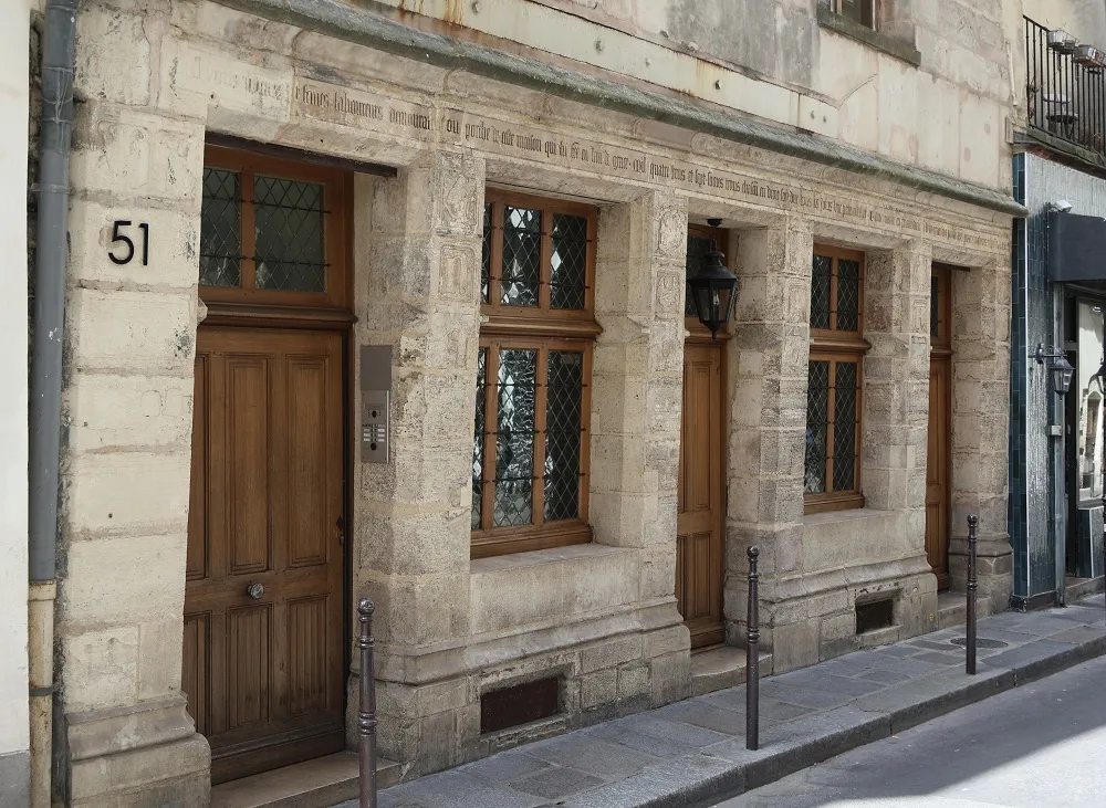 Façade en pierre d'une maison identifiée par le numéro 51. Murs en pierre, porte et fenêtres en bois. Photographie prise de la rue de trois-quarts. 