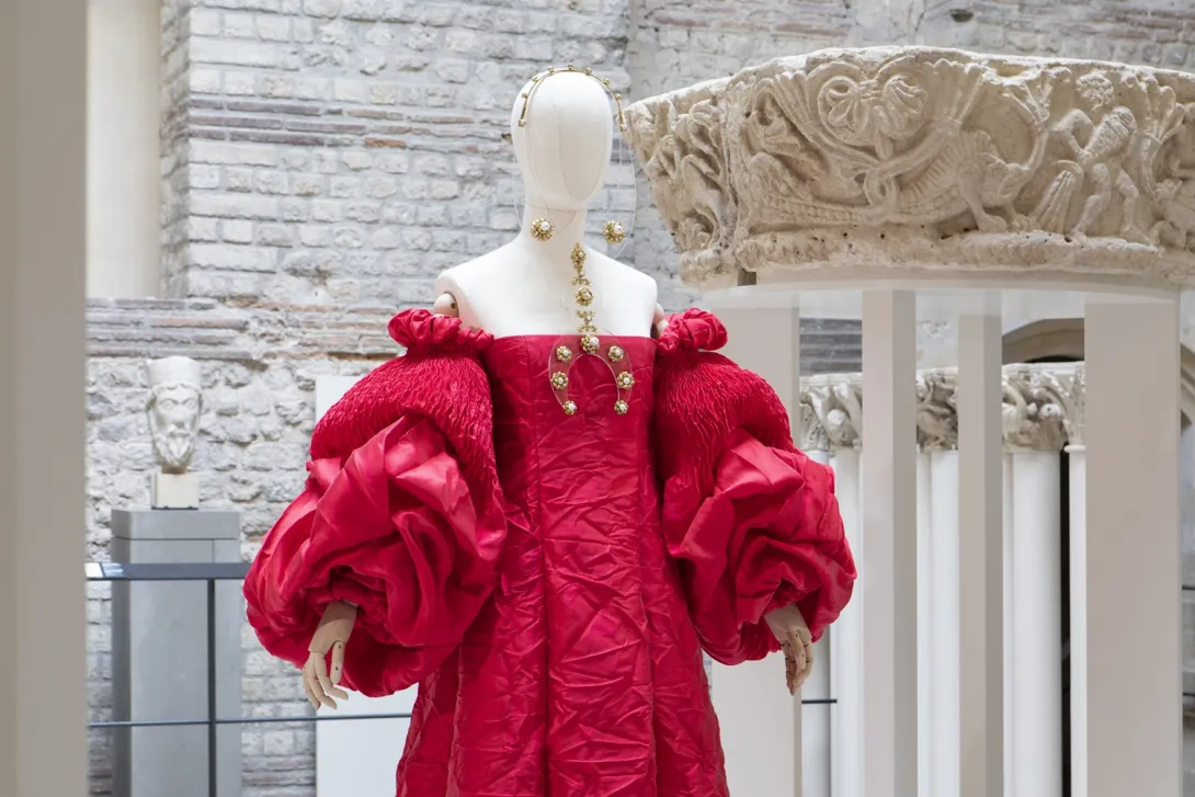 Vue en buste d'une robe rouge placée sur un mannequin dans un décor de sculptures