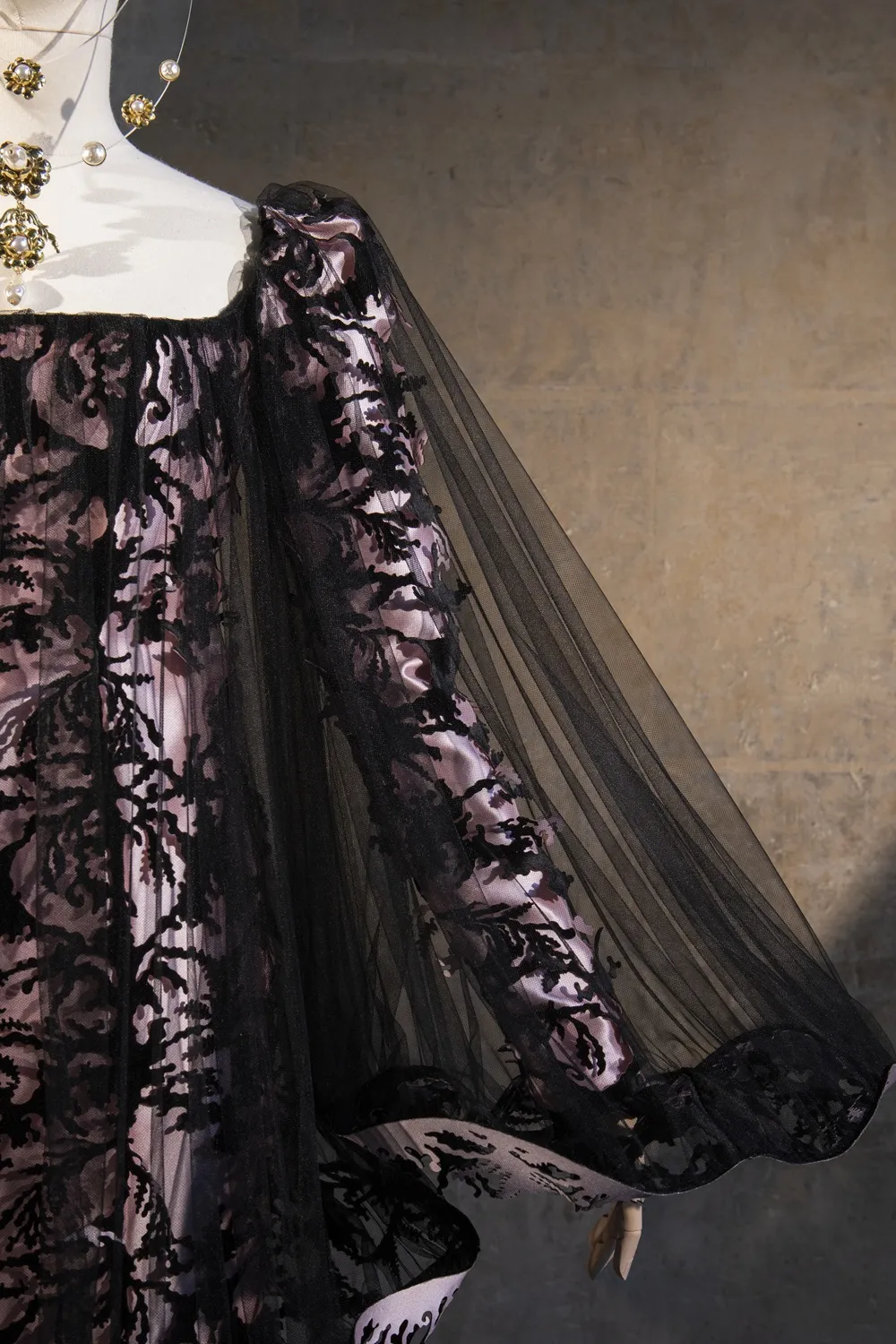 Détail d'une robe noire posée sur un mannequin. Robe brodée en transparente avec un voile noir.