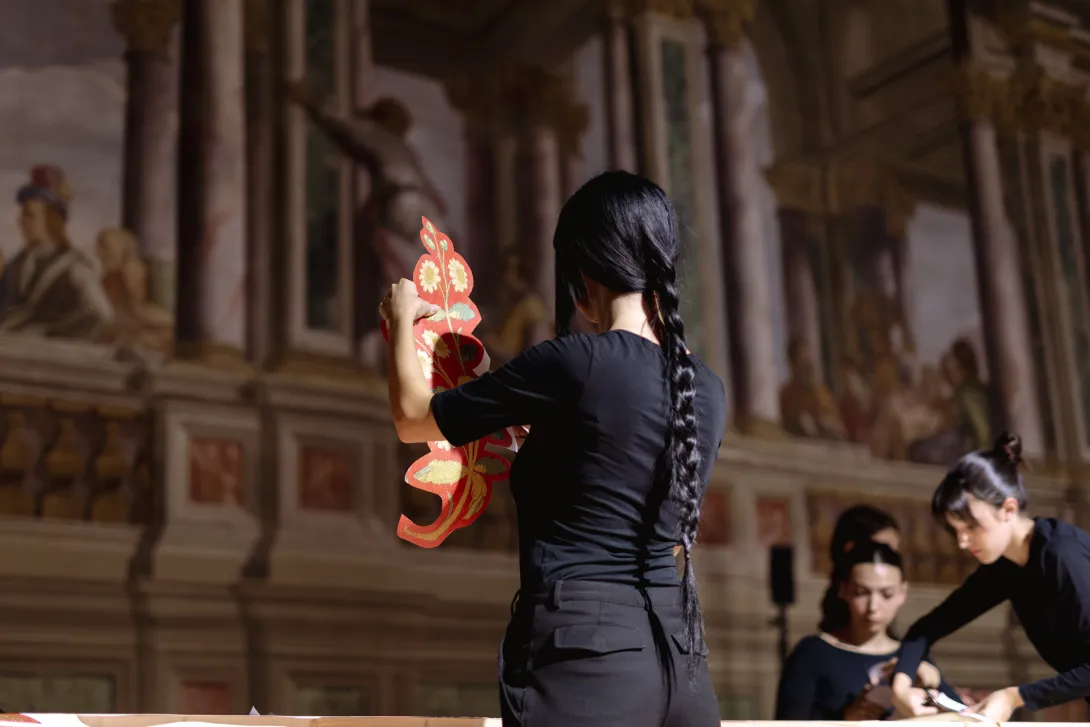 Une femme de dos découpe une forme en papier. 