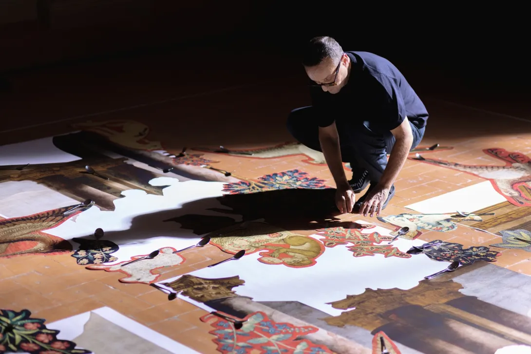 Un homme est accroupi devant des formes en papier découpées. 