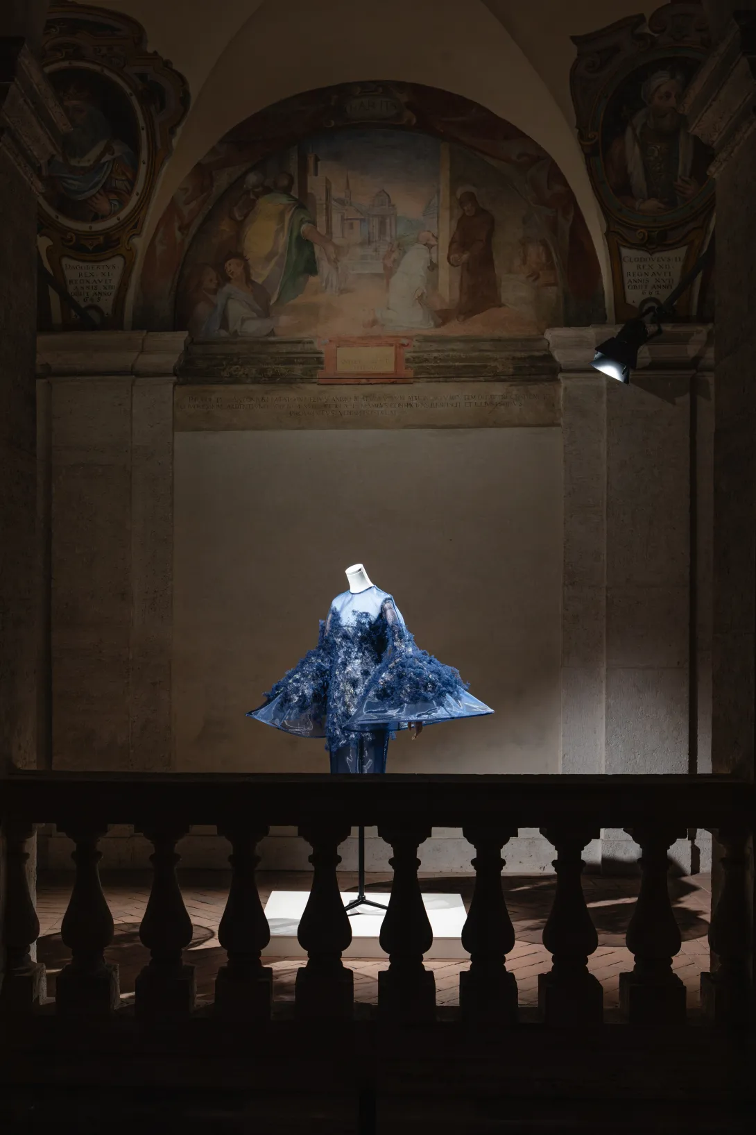Robe bleue éclairée par des spots dans un décor de pénombre. 