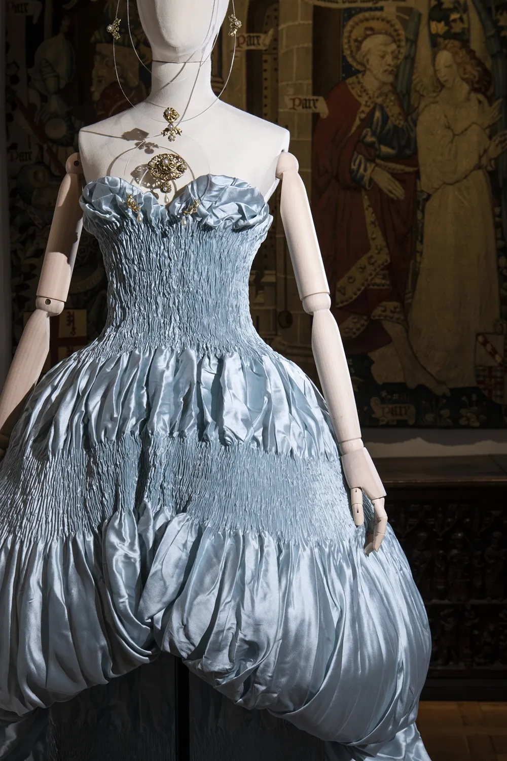 Robe du soir bleue avec, en arrière-plan, des tapisseries. 