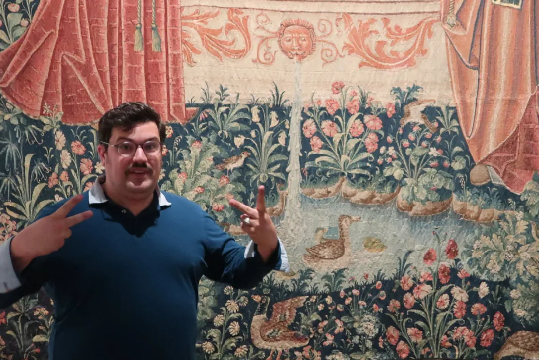 Un homme devant une tapisserie médiévale signe un mot en langue des signes française