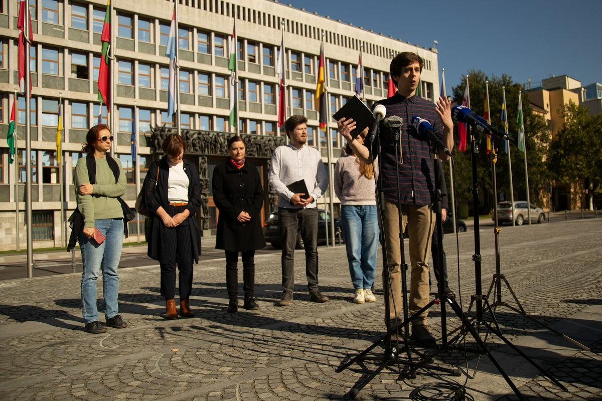 Filip stoji pred mikrofoni različnih medijev na Trgu republike, v ozadju pa predstavniki in predstavnice drugih NVO