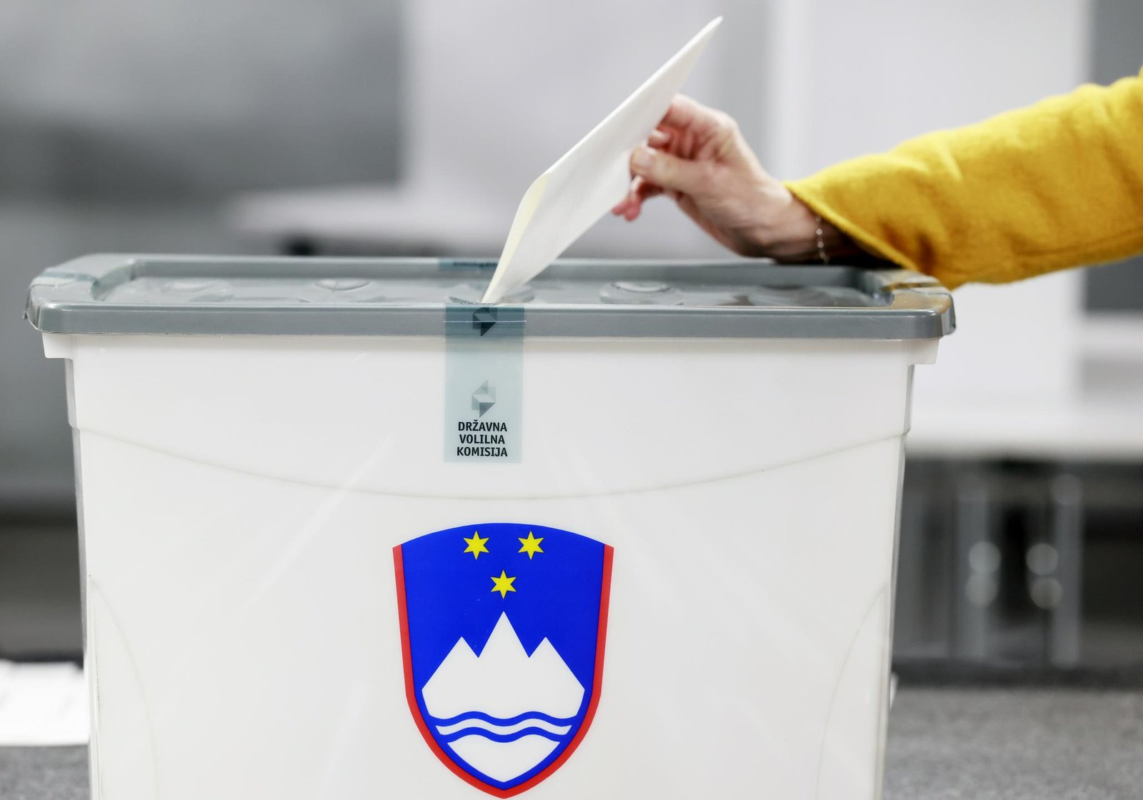 Volilna skrinjica, na kateri je grb Republike Slovenije, roka vanjo odlaga listič