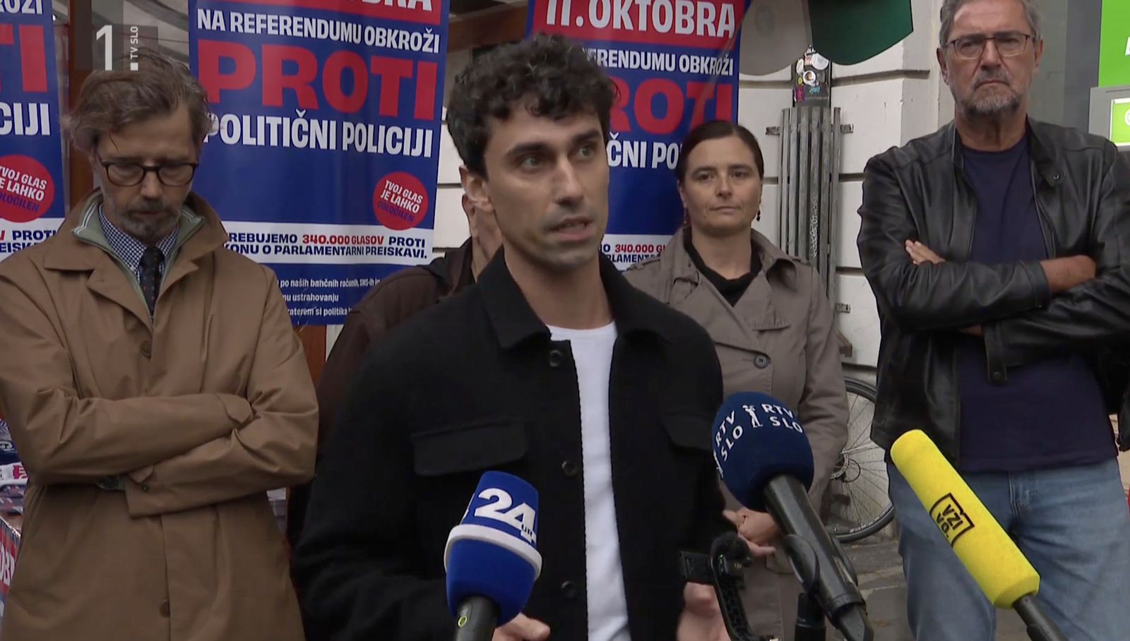 Nejc pred stojnico proti politični policiji v centru Ljubljane, v ozadju ostali pobudniki referenduma.