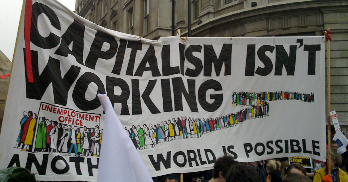 fotografija z demonstracij, vidi se le ogromen transparent, na njem je napis: capitalism isn't working, another world is possible