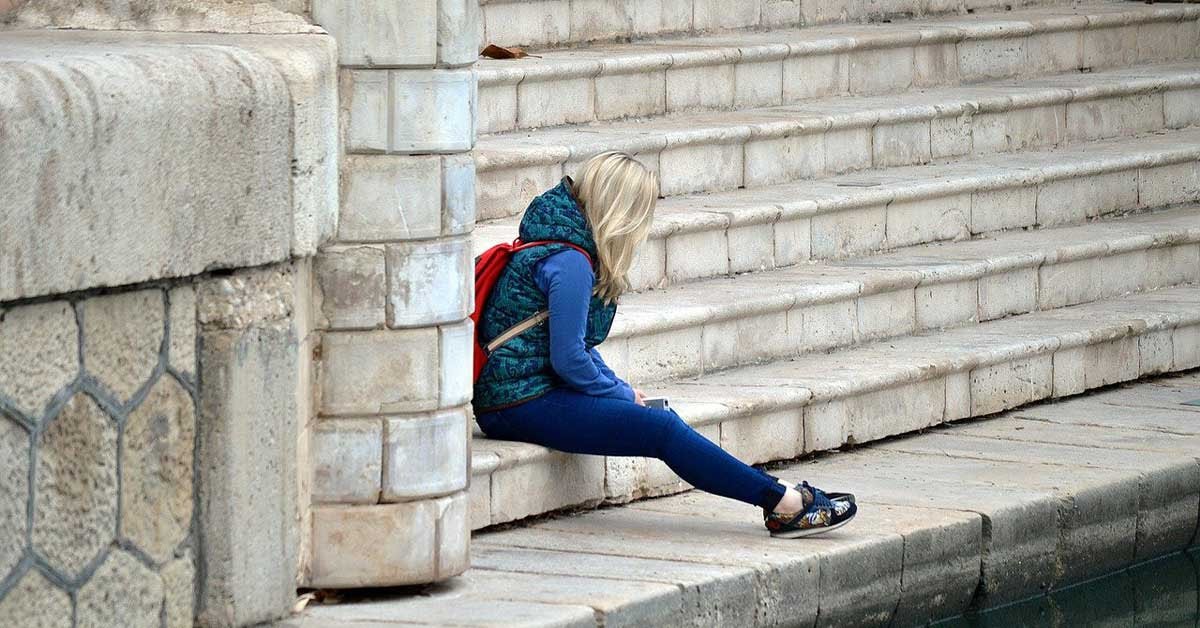 Ženska sedi sama na stopnicah ob vodi.