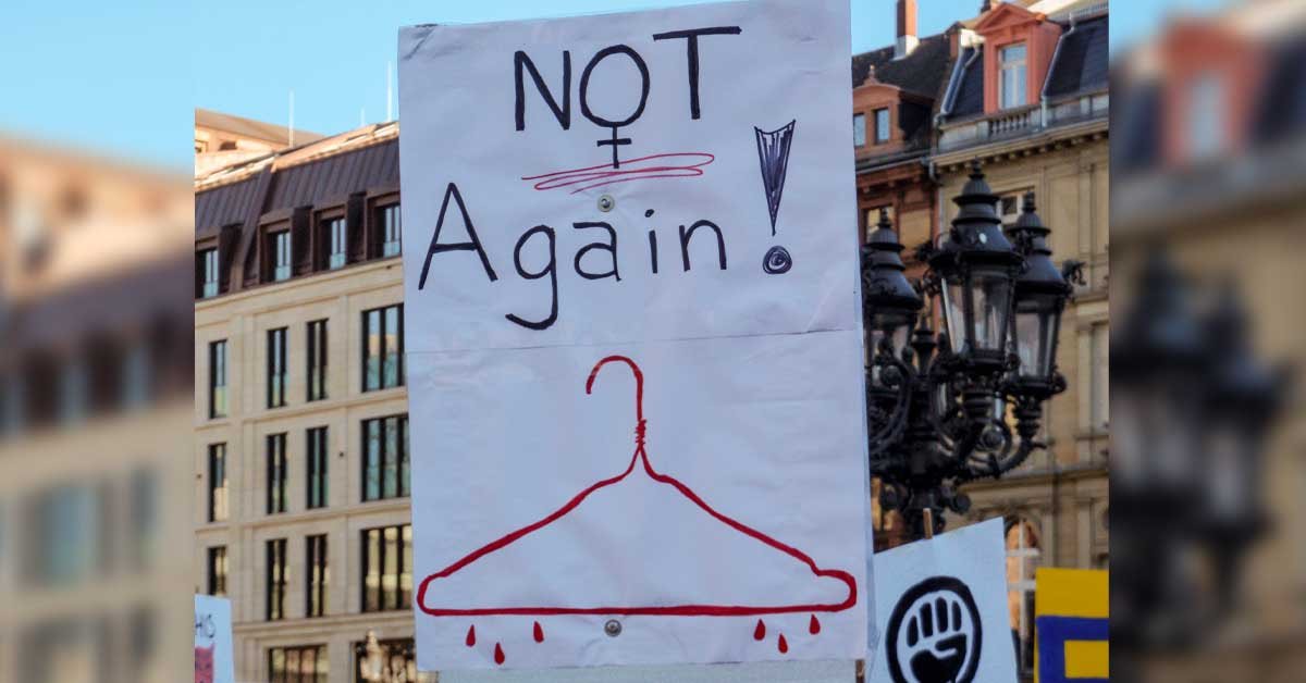 Protestni plakat, na katerem piše Not again, spodaj pa je narisan krvav obešalnik.