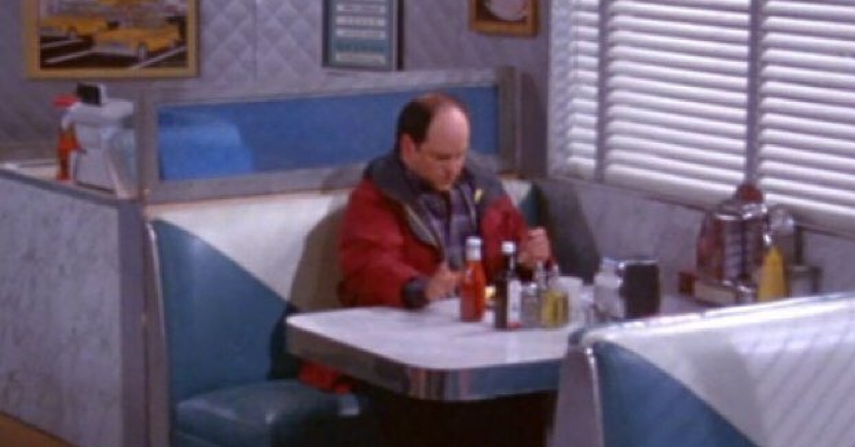 George Costanza iz televizijske serije Seinfeld osamljen sedi za mizo v baru.