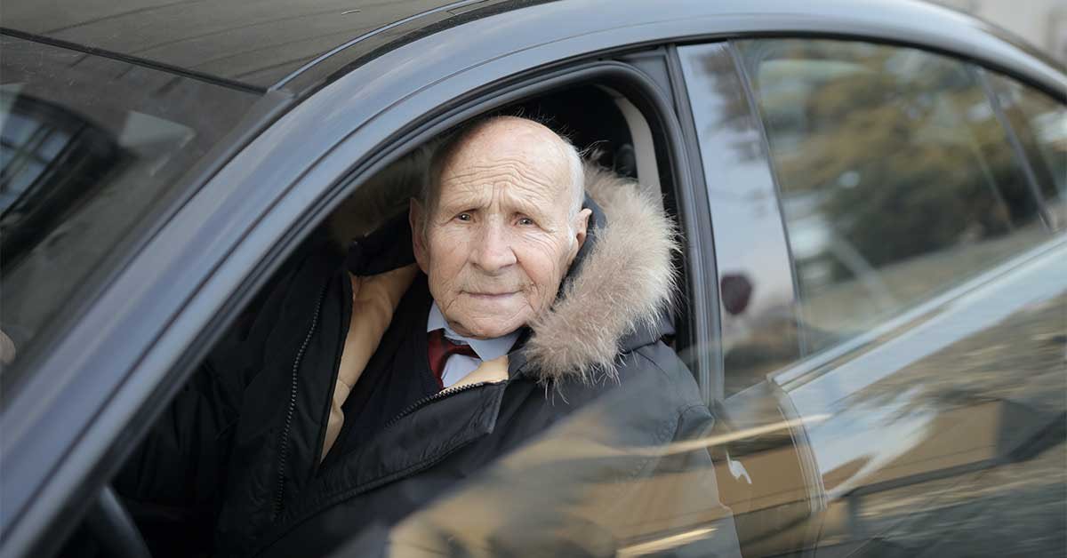 Starejši voznik gleda v kamero, ko izstopa iz vozila.