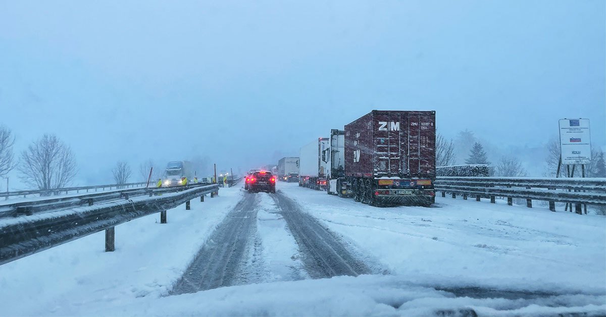 Fotografija večdesetkilometrske kolone vozil, ki so v ponedeljek nastale na vseh koncih države. Na voznem pasu so tovorna vozila, na prehitevalnem pa je kolona osebnih avtomobilov v močnem sneženju.