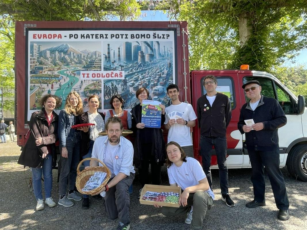 Fotografija z novinarske konference Glas ljudstva z osebami, ki pozirajo. V ozadju je vozilo s plakatom, na katerem piše Evropa – po kateri poti bomo šli? Ti odločas.