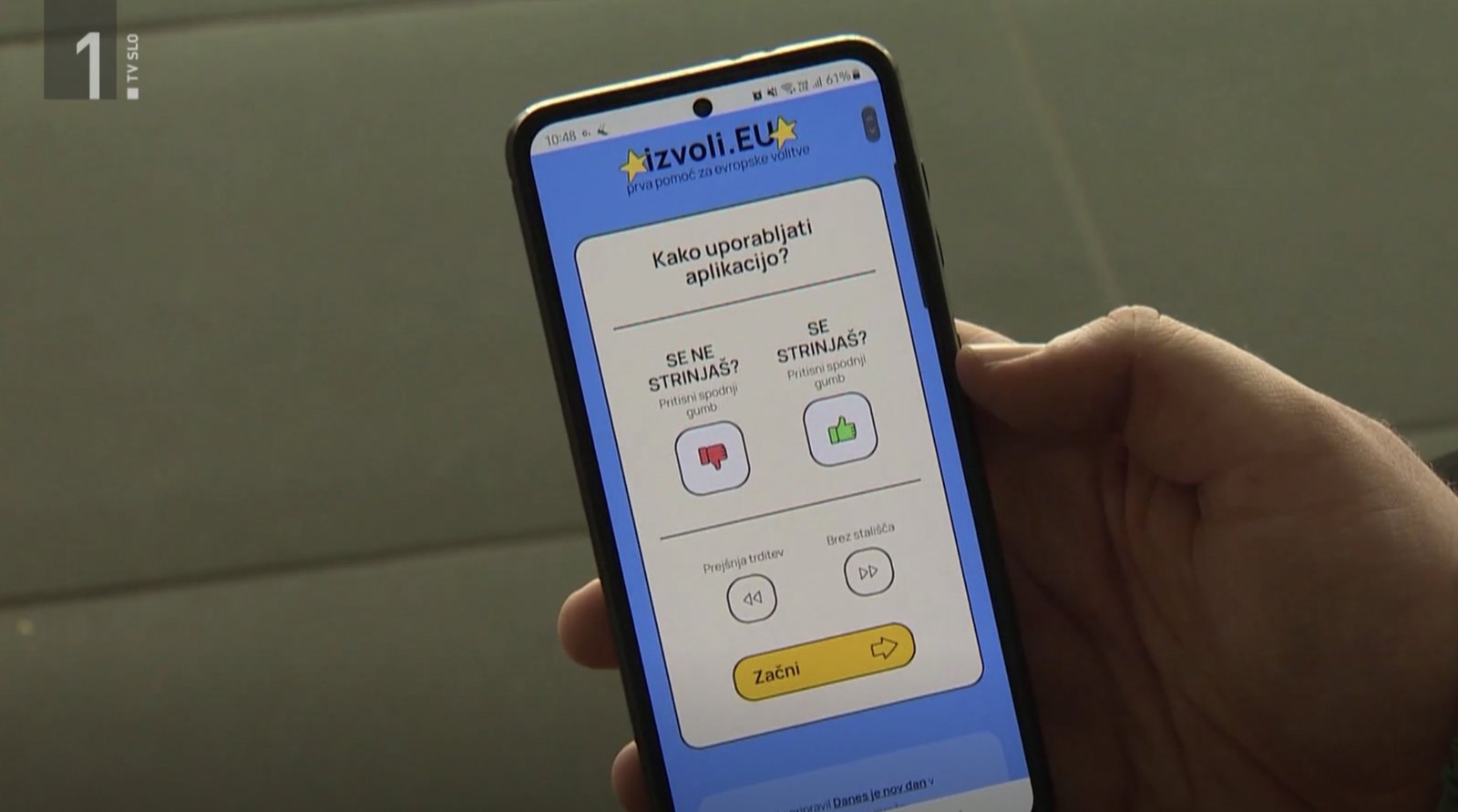 Zajem zaslona iz televizijskega prispevka o Izvoli.eu, na katerem je telefon z odprto aplikacijo Izvoli.eu