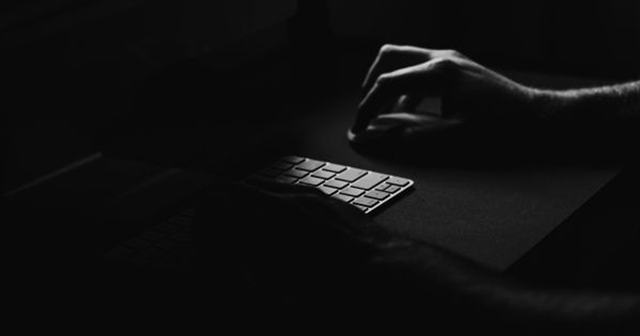 Temna fotografija roke, ki tipka po tipkovnici računalnika, kar simbolizira zasebnost na spletu.