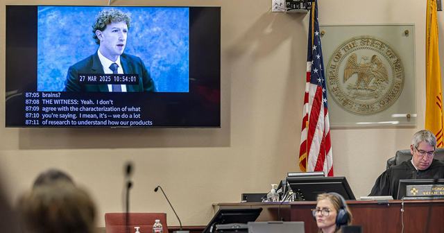 Na fotografiji je sodna dvorana, kjer sodnik sedi za mizo, na zaslonu pa je prikazan posnetek zaslišanja Marka Zuckerberga z vidnimi podnapisi njegove izjave.