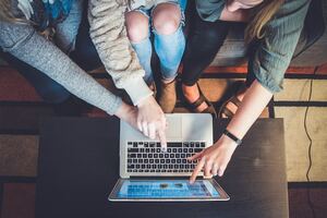 trois personnes pointant à un ordinateur en signe de collaboration