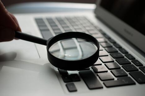 une maine tenant une loupe et fixant un clavier d'ordinateur