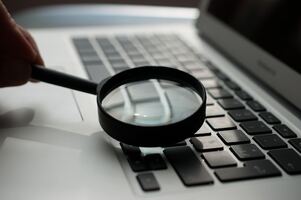 une maine tenant une loupe et fixant un clavier d'ordinateur