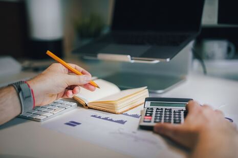 homme devant un ordinateur et tenant une calculatrice dans ses maina