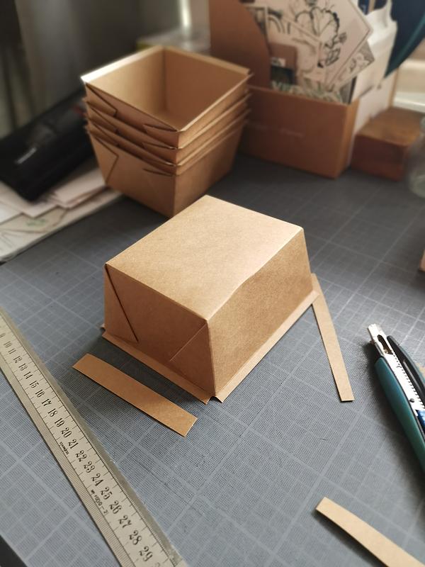 Une petite boîte en carton, type pour de la vente à emporter, retournée sur un plan de travail. On peut voir d'autres boîtes sur le bureau. Le pliage du couvercle de la boîte a été retiré et coupé sur les bords.