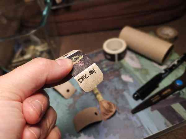 Une main qui tient un petit rectangle de carton avec du masking tape collé dessus et du texte "DMC 841"