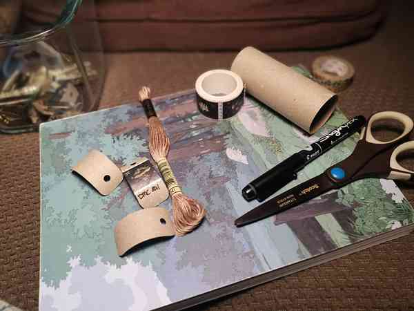 Des petits bouts de carton, du masking tape, une paire de ciseaux et un feutre noir posé sur un magazine.