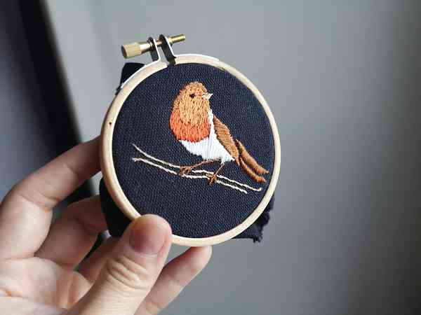 Une main qui tient une broderie de rouge-gorge