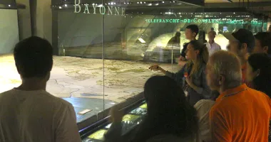 Une conférencière montre la maquette de Bayonne à un groupe de visiteurs.