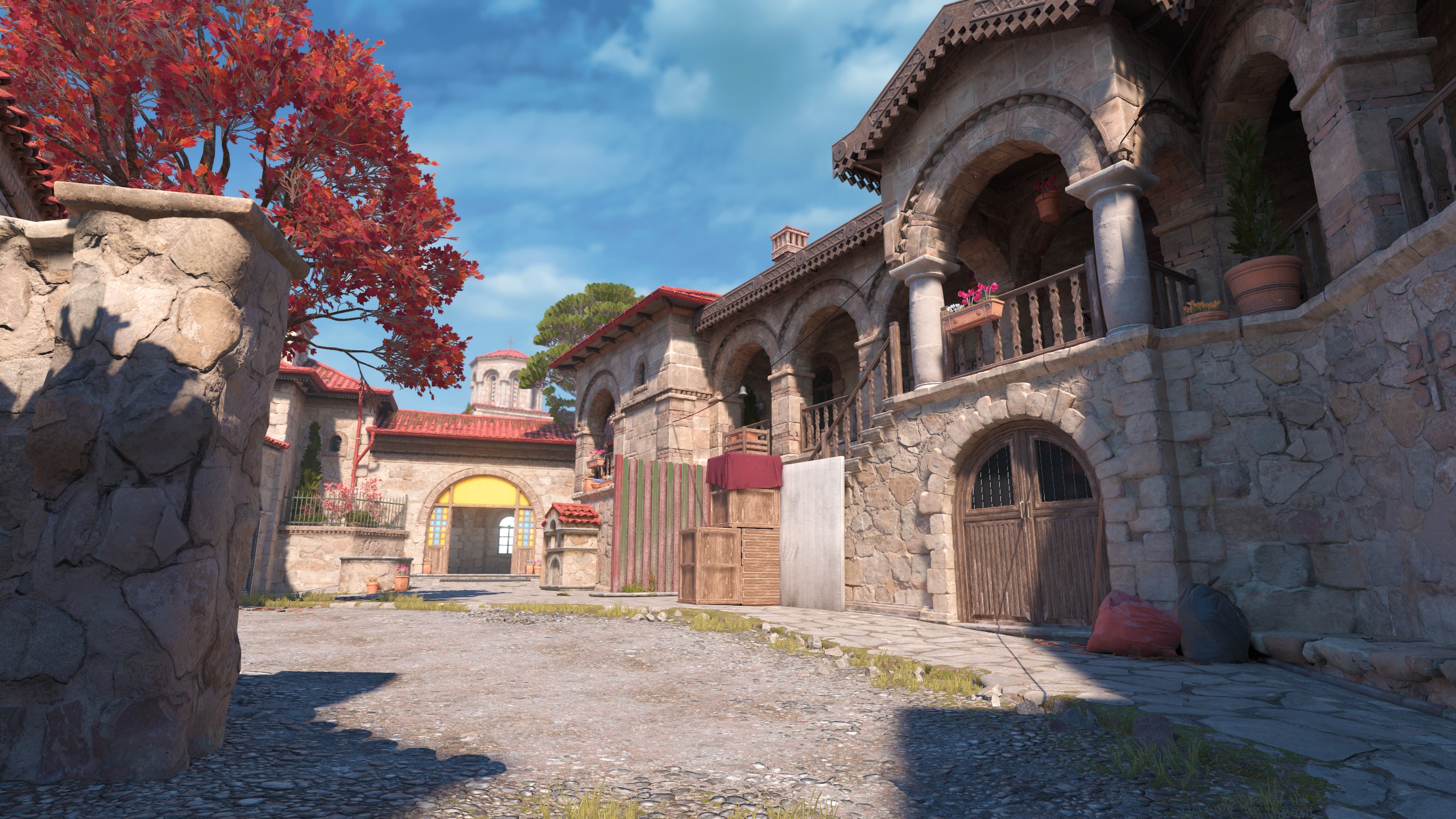 Cour extérieure de Boulder dans Counter-Strike 2 : arcades de pierre, palissade en bois et sacs posés au sol