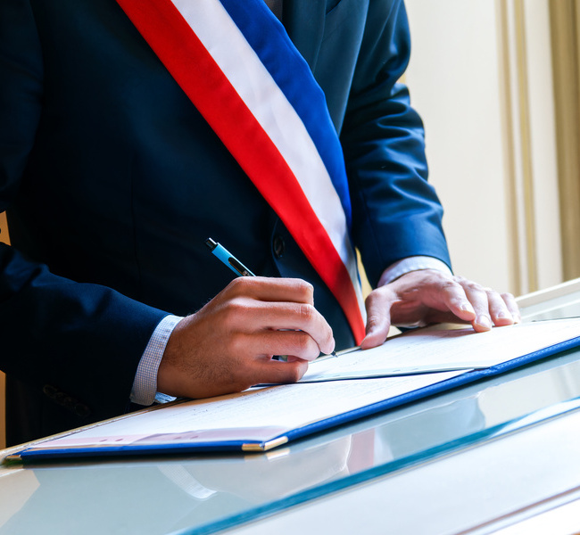 Signature officielle d’un acte de mariage civil par un élu portant l’écharpe tricolore française, symbole de la République et de l’union légale
